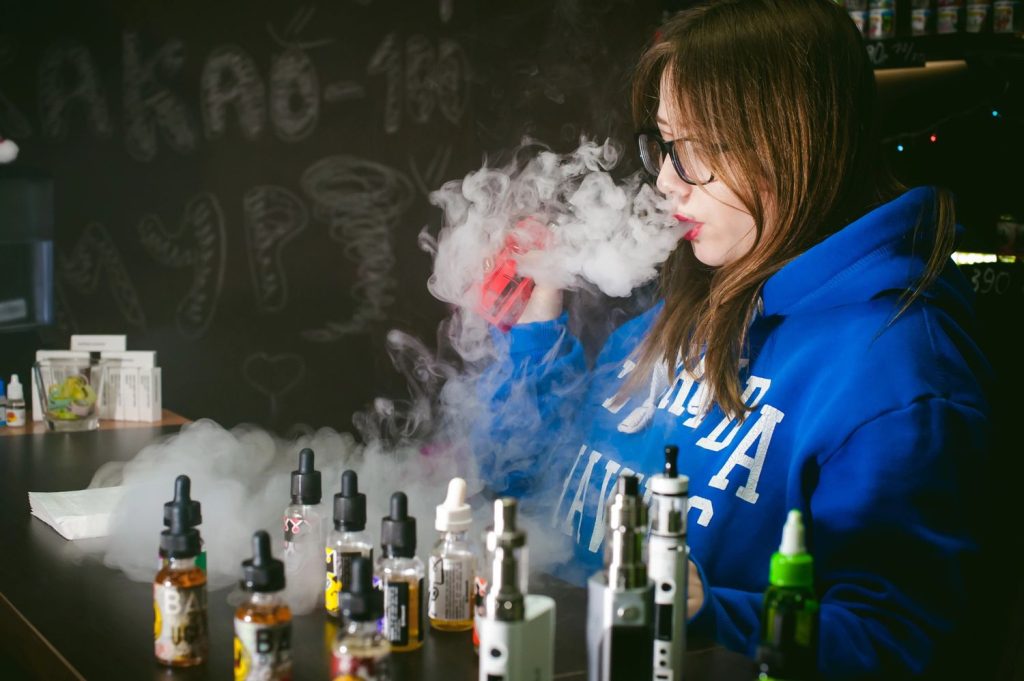 Woman vaping with various e-liquids and devices, showcasing a trendy vape shop in Tulsa.