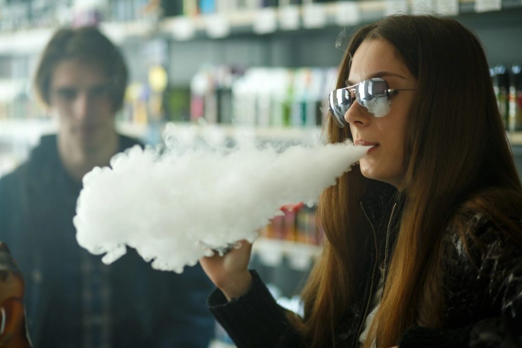 Woman vaping with a cloud of smoke in a modern vape shop in Tulsa, showcasing vaping products.