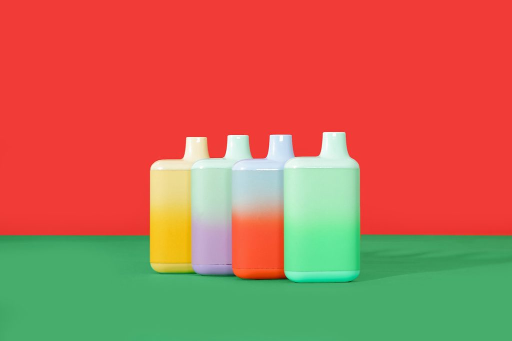 Four pastel-colored, large disposable vapes Tulsa standing on a green surface with a striking red background.