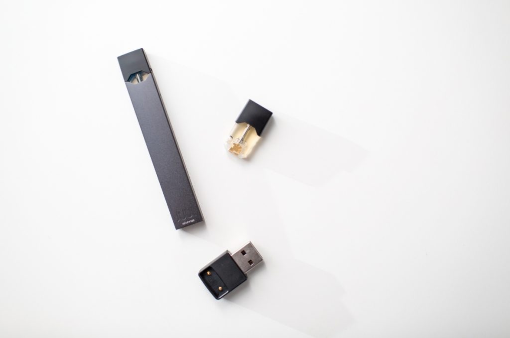 Close-up of a sleek vape mod, a pod, and its USB charger on a white background. Shop high-quality vape mods Tulsa.