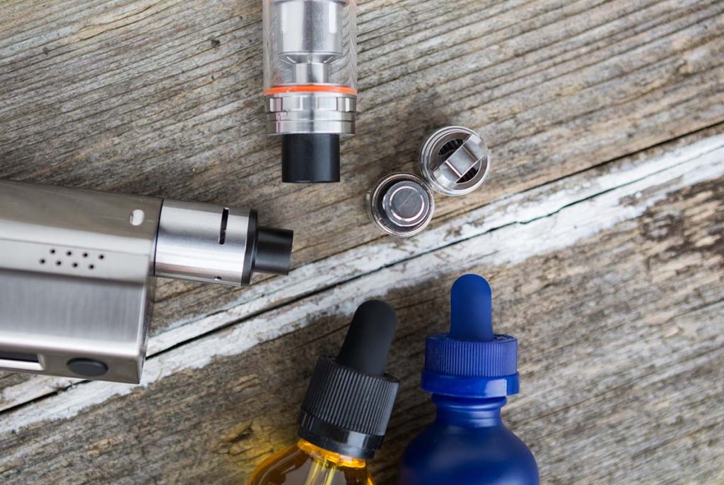 Vaping tank, coils, and bottles of e-liquid on wood, accessories for a disposable vapes Tulsa user.