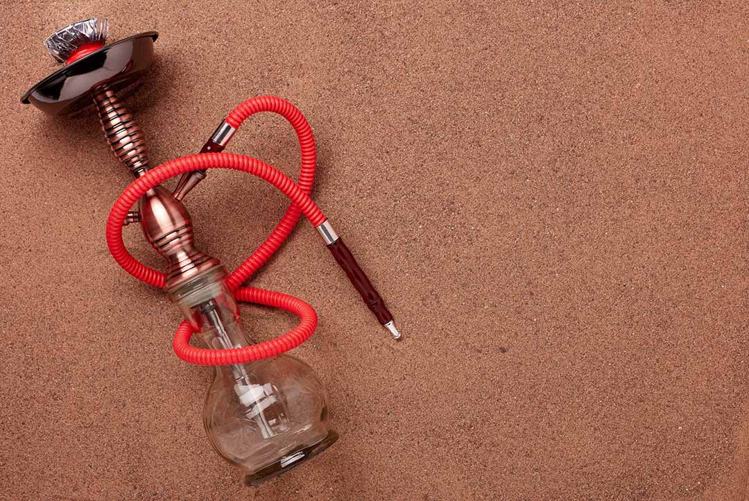 Elegant glass and bronze hookah with a red hose on a brown textured background for the shisha store Tulsa blog.