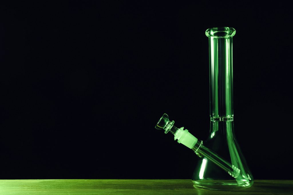 Classic beaker-style glass pipes from Tulsa, illuminated with green glow against black background, ideal for enthusiasts seeking quality craftsmanship.