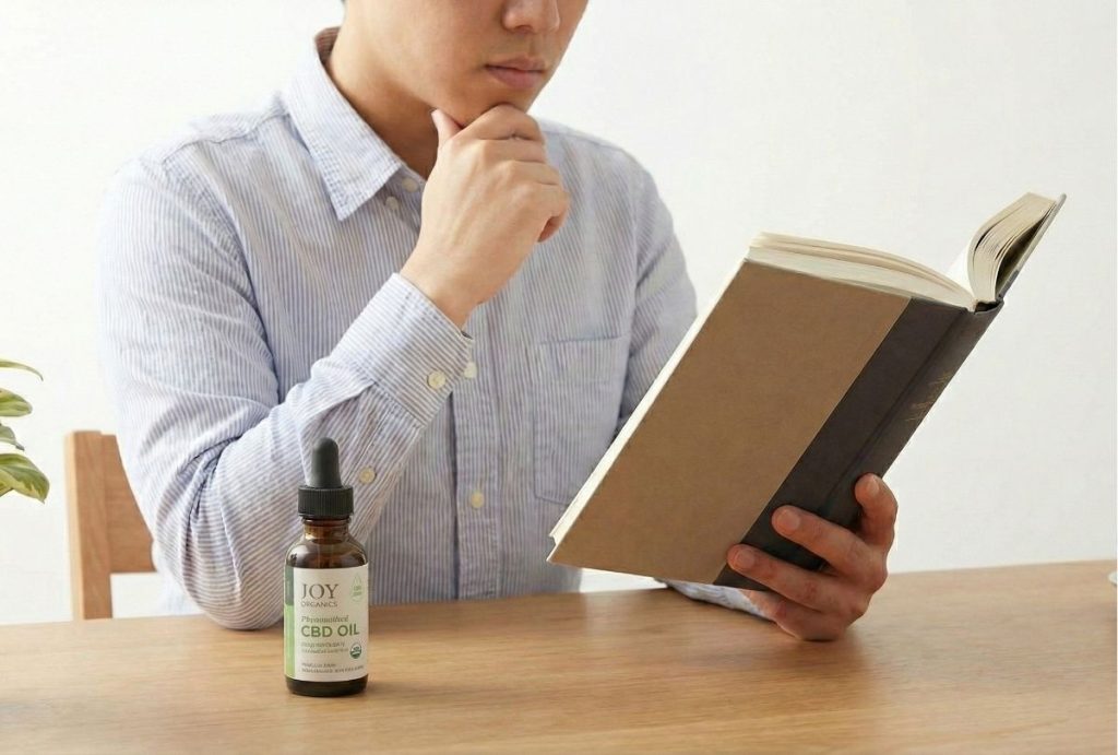 A focused man reading a book with Joy Organics CBD Oil on the table, available at a cbd store sapulpa.