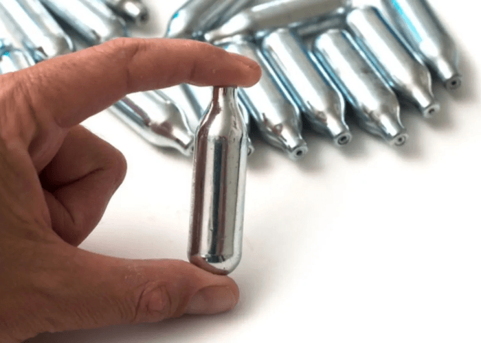 A hand holding a single silver N2O whip cream charger for a cream siphon, in Tulsa, Oklahoma.