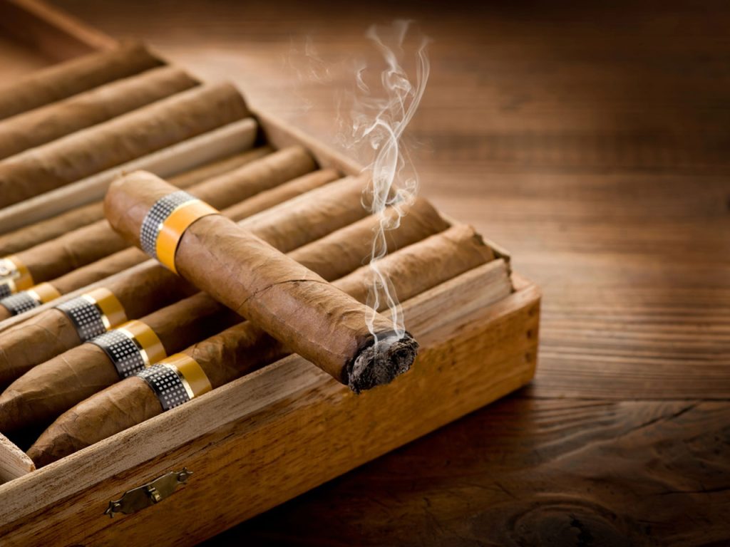 Premium hand-rolled cigars in a wooden humidor at a cigar shop Tulsa, featuring a smoking cigar with natural leaf wrap.