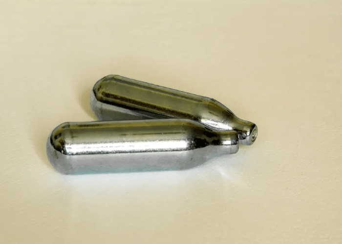 Two silver whip cream chargers for N2O, lying on a light-colored surface in Tulsa, OK.