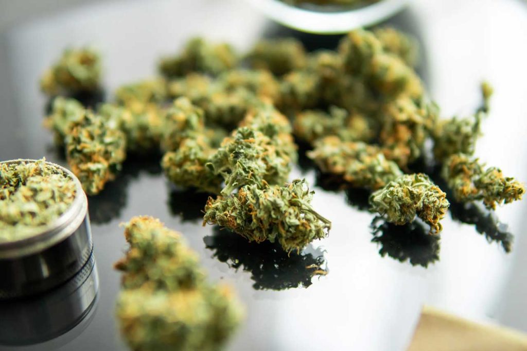 Premium hemp flower buds and a metal grinder on a reflective table at a top-rated delta 8 store Tulsa location.