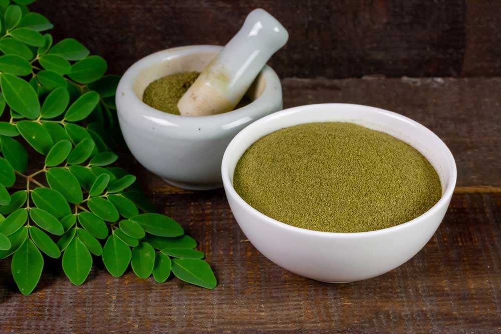 A mortar and pestle grinding green herbal powder next to fresh leaves from a trusted kratom shop Tulsa source.
