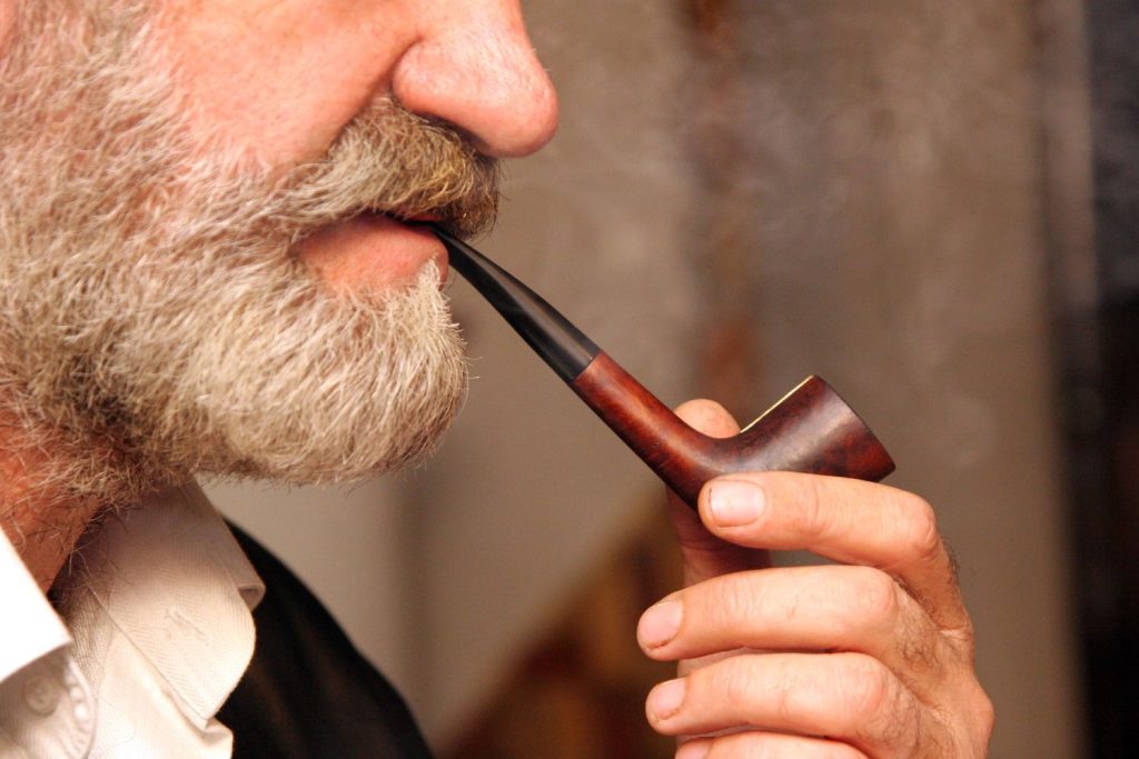 Elderly bearded man smoking a wooden pipe, showcasing premium products from our tobacco shop in Tulsa.