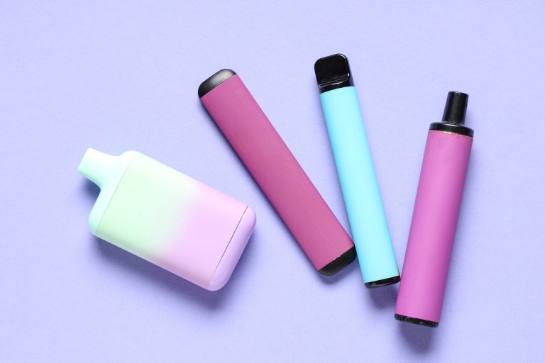 Four colorful disposable vape devices in pastel purple, pink, teal, and gradient green-to-purple arranged on a light purple background – SMACK BOYZ premium vapes available at Tulsa's top vape shop.