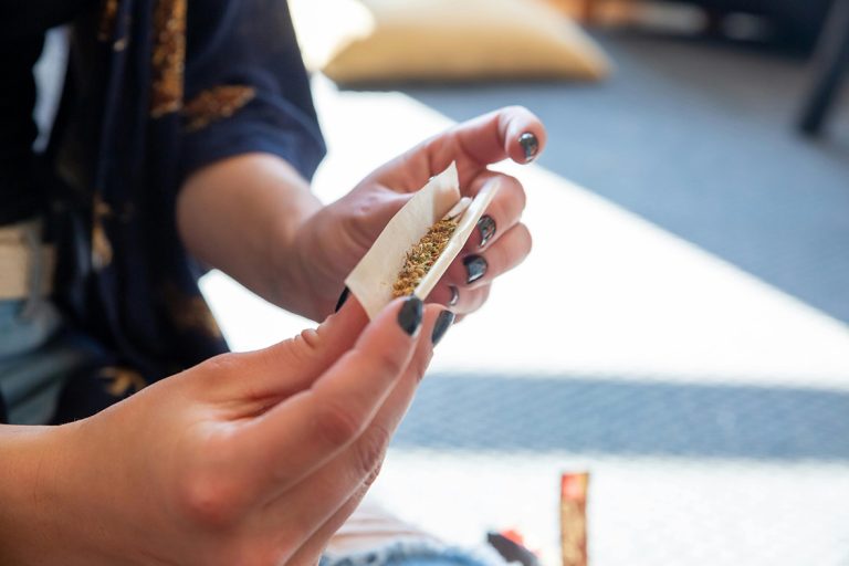 Close-up of hands with dark nail polish holding a white rolling papers Tulsa to prepare a roll-up.