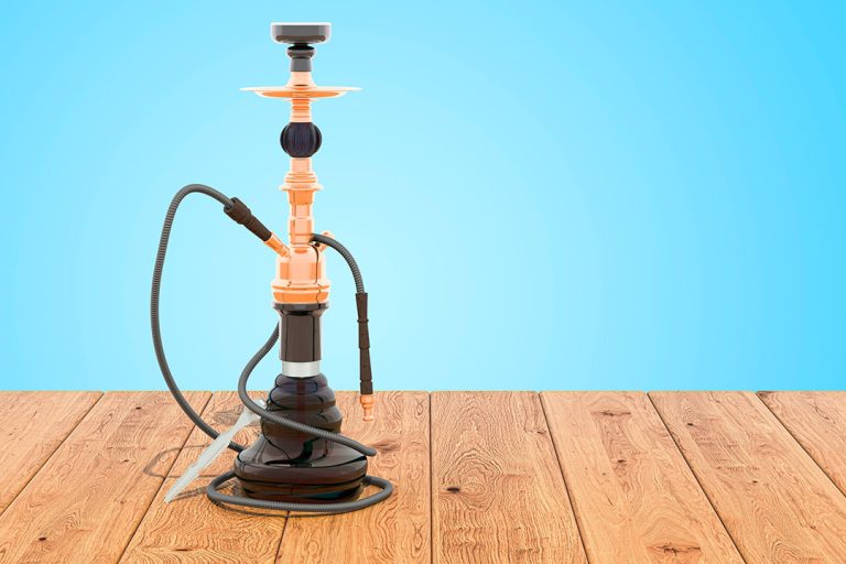 Tall, detailed copper-tone hookah with a black base and hose on a wooden table, offered by shisha store Tulsa.