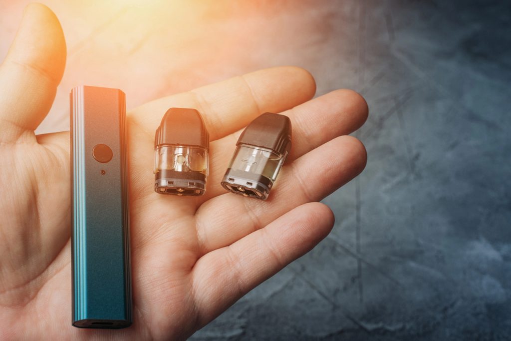 Hand holding teal vape device with two nicotine pods in Tulsa, showcasing refillable pods for smooth vaping experience