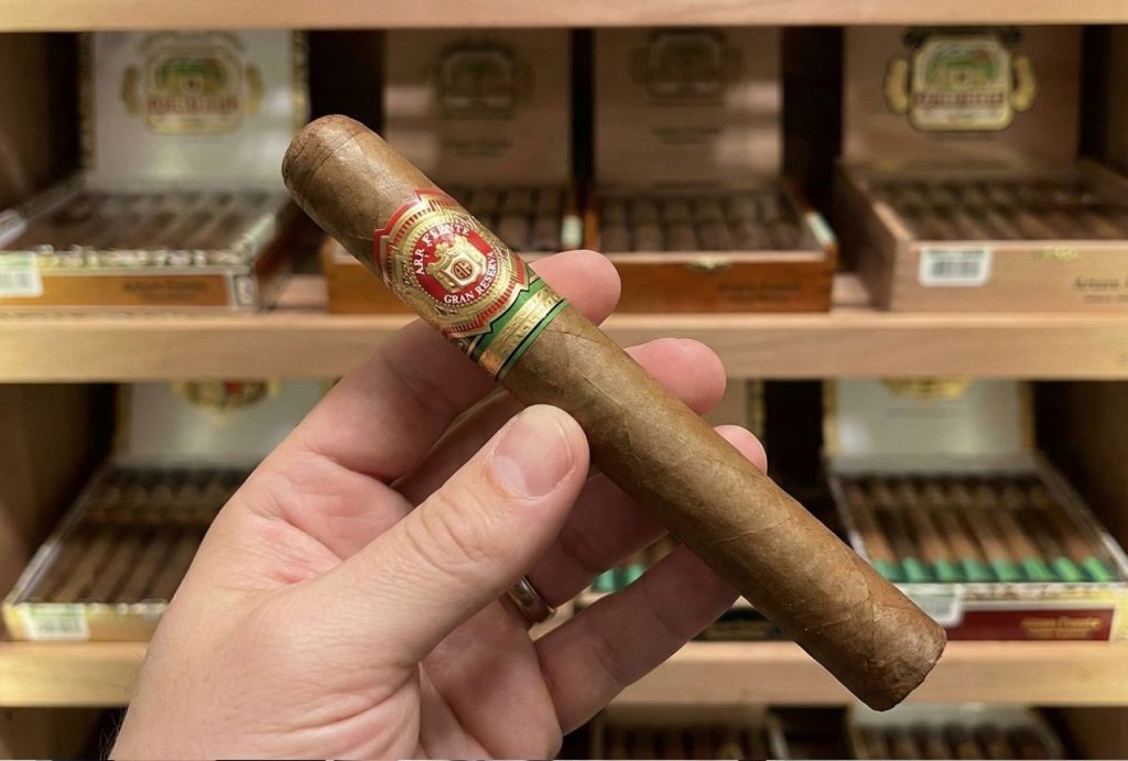 Close-up of a hand holding a premium Arturo Fuente Gran Reserva cigar inside the humidor of a cigar shop Tulsa
