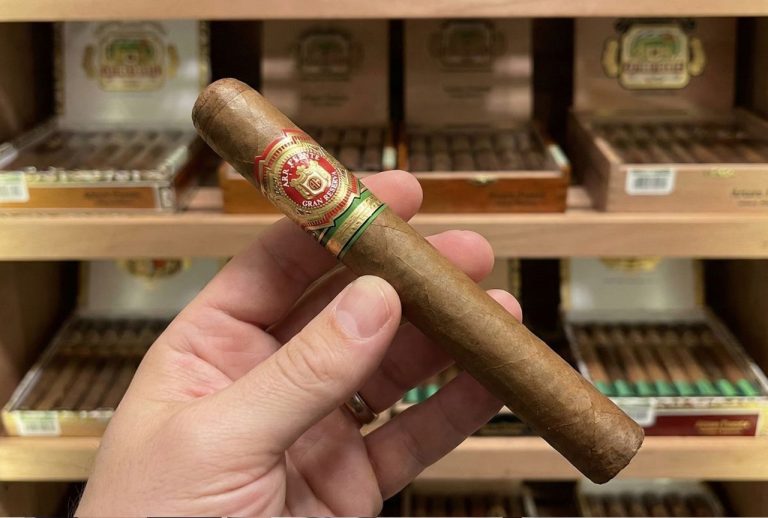 Close-up of a hand holding a premium Arturo Fuente Gran Reserva cigar inside the humidor of a cigar shop Tulsa