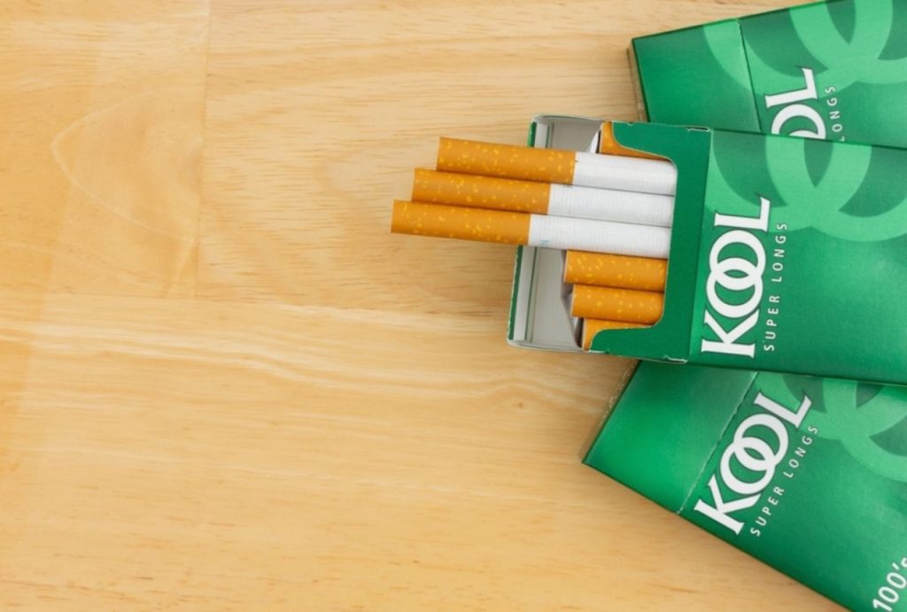 An open pack of green Kool Super Longs 100s on a wooden table, a classic brand found at a cigarette shop Tulsa.