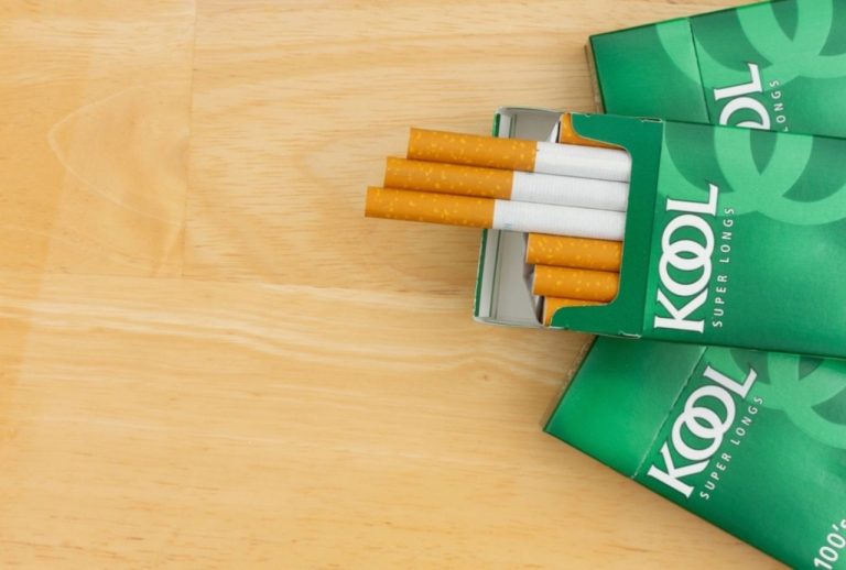 An open pack of green Kool Super Longs 100s on a wooden table, a classic brand found at a cigarette shop Tulsa.