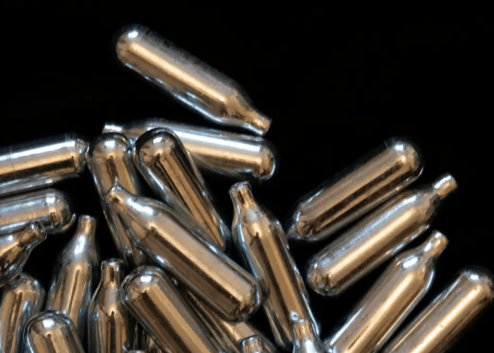 A bulk collection of small silver whip cream chargers, on a black background in Tulsa, OK.