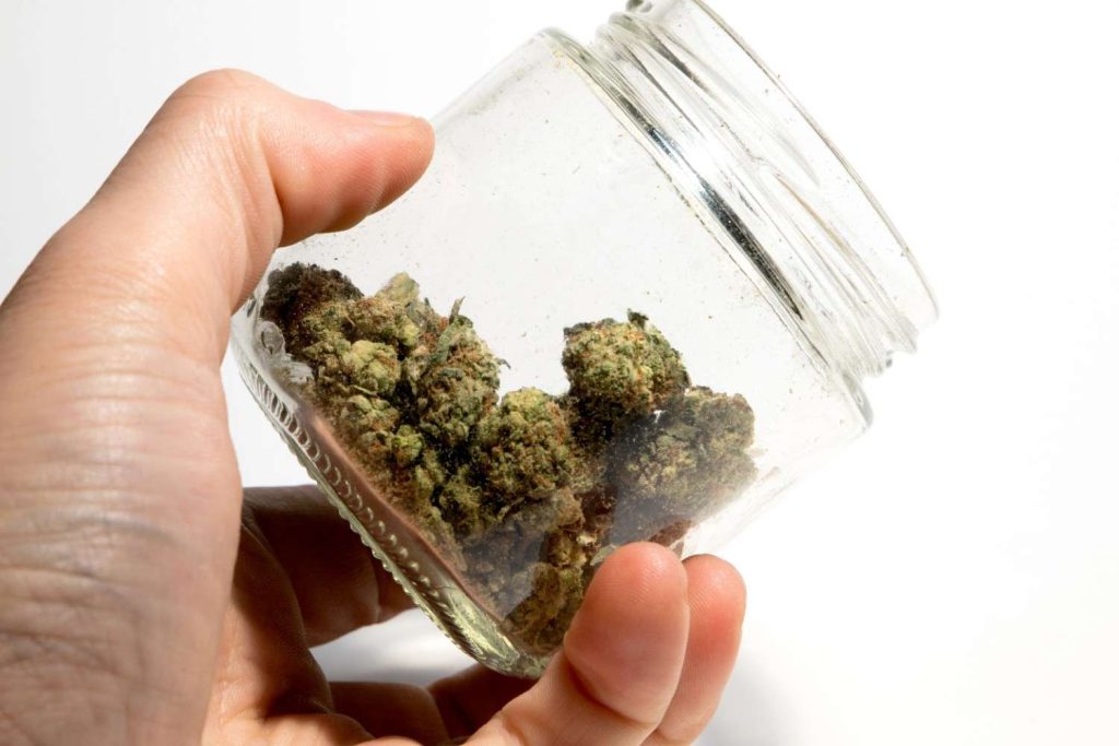 Hand holding a clear glass jar filled with premium cannabis buds inside a local delta 8 store tulsa retail shop.