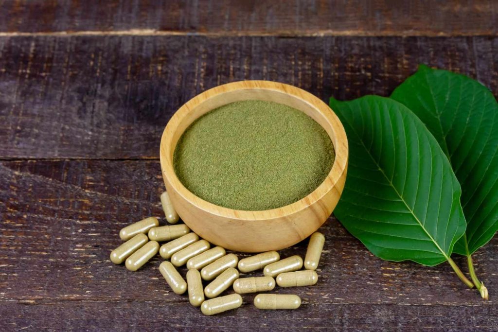 Finely milled powder in a wooden bowl with capsules and green leaves, representing top kratom retail Tulsa shop options.