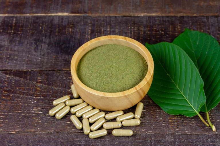 Finely milled powder in a wooden bowl with capsules and green leaves, representing top kratom retail Tulsa shop options.